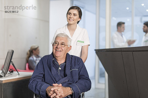 Krankenschwester mit Patient im Rollstuhl an der Klinikrezeption