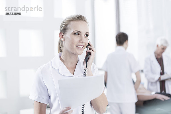Krankenschwester im Krankenhaus mit Unterlagen am Telefon