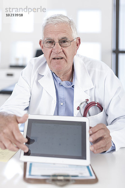 Seriöser Oberarzt am Schreibtisch mit digitalem Tablett