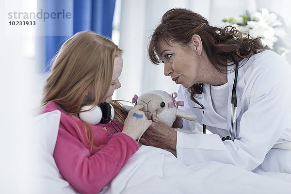 Arzt kommuniziert mit einem Mädchen  das im Krankenhausbett liegt