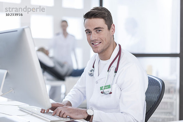 Porträt eines lächelnden Arztes am Schreibtisch bei der Arbeit am Computer