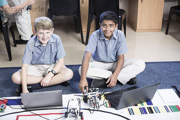 Zwei lächelnde Schüler mit Laptops im Robotikunterricht