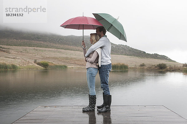 Paar im Regen stehend auf Holzsteg mit Regenschirmen