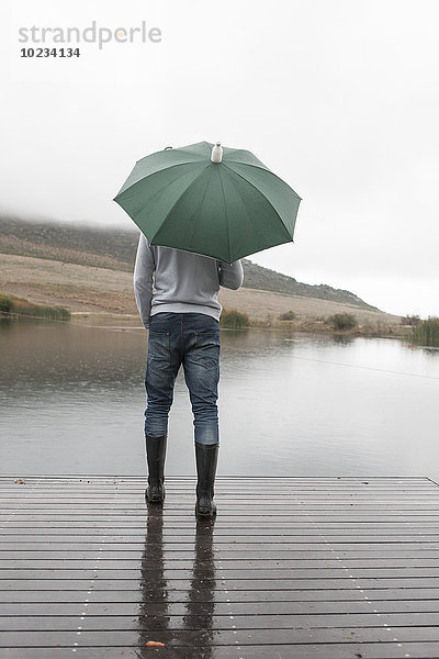 Mann im Regen stehend auf Holzsteg mit grünem Schirm