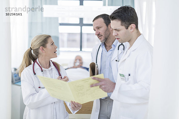 Drei Ärzte mit Bericht in einem Krankenhauszimmer
