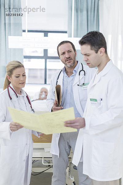 Drei Ärzte mit Bericht in einem Krankenhauszimmer