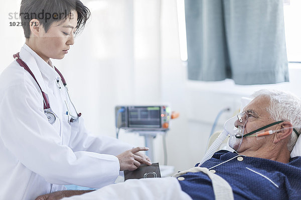 Arzt  der den Blutdruck eines älteren Mannes mit Sauerstoffmaske in einem Krankenhaus nimmt.