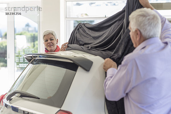 Seniorenpaar enthüllt ein neues Auto beim Autohändler