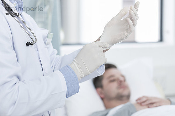 Arzt zieht Handschuhe an  Patient im Hintergrund