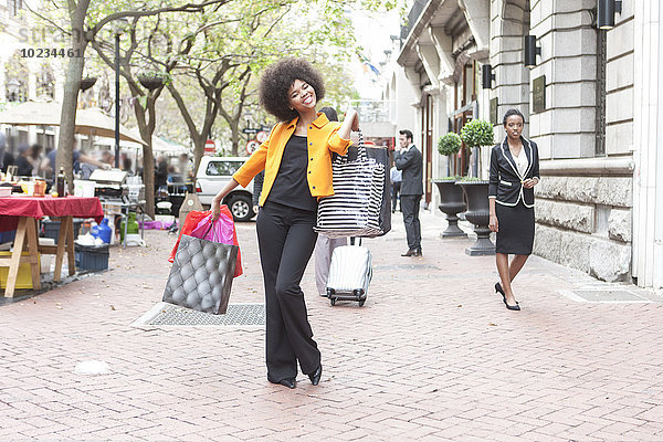 Fröhliche junge Frau posiert mit ihren Einkaufstaschen auf dem Bürgersteig