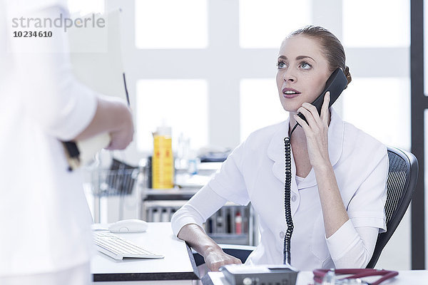 Krankenschwester am Schreibtisch am Telefon mit Blick auf den Arzt