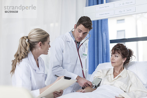 Arzt und Krankenschwester untersuchende Frau im Krankenhausbett