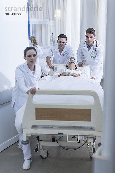 Krankenhauspersonal schiebt Bett mit Patient auf dem Boden