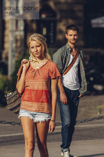 Porträt einer jungen Frau  die auf der Straße geht  während ihr Freund im Hintergrund steht.