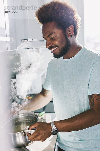 Lächelnder Mann hält Kochtopf mit heißem Wasser.