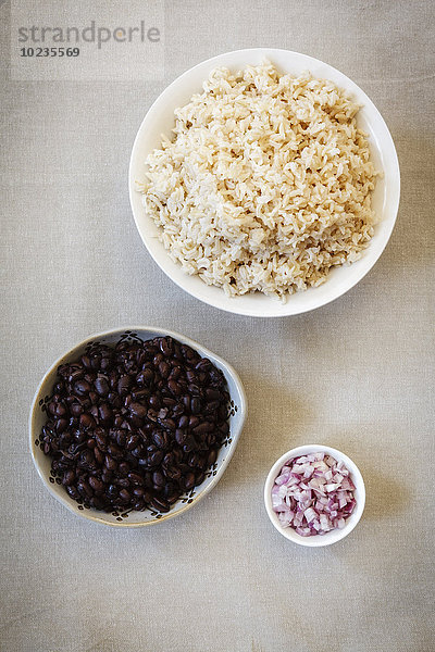 Schalen mit Zwiebelwürfeln  gekochtem Reis und schwarzen Bohnen