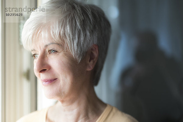 Porträt einer lächelnden Seniorin mit Blick durchs Fenster