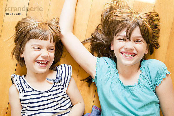 Porträt zweier lachender Schwestern auf Holzboden liegend
