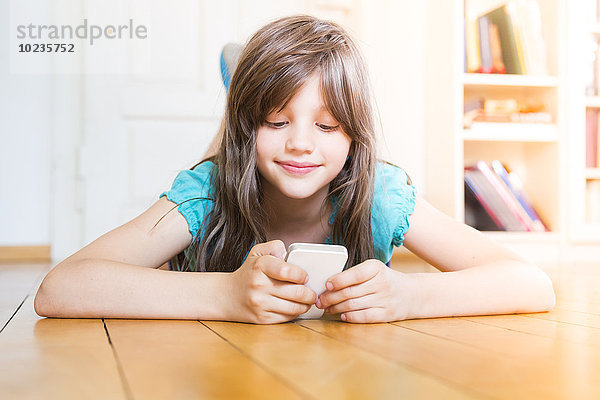 Lächelndes Mädchen auf Holzboden liegend mit Smartphone