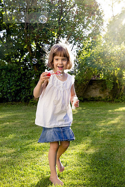 Kleines Mädchen spielt mit Seifenblasen im Garten