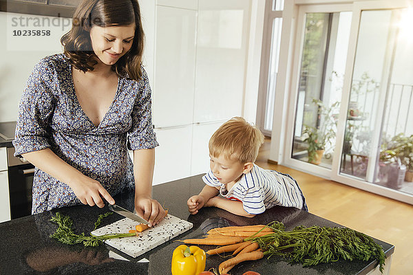 Schwangere Frau  die mit ihrem Sohn in der Küche Gemüse schneidet.