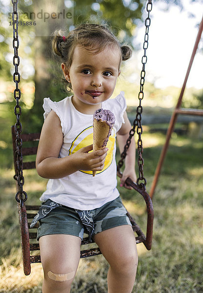 Porträt eines glücklichen kleinen Mädchens  das auf einer Schaukel sitzt und Eis isst.