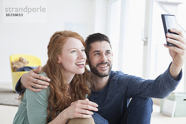 Lächelndes junges Paar  das einen Selfie mit Smartphone im Wohnzimmer nimmt.