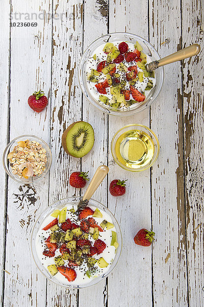 Erdbeer-Kiwi-Joghurt mit Getreide  Chiasamen  Agavendicksaft in Glasschale auf Holz