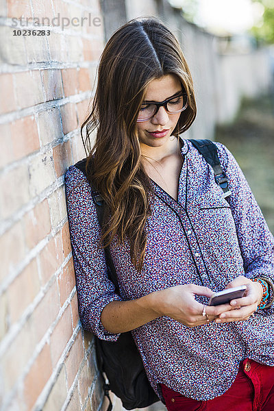 Brünette junge Frau mit Brille beim Blick auf das Handy