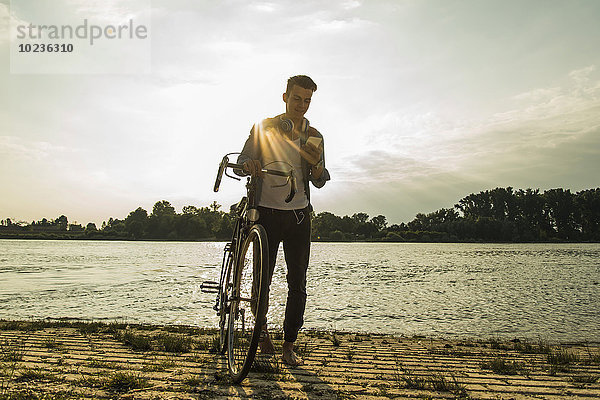 Junger Mann mit Fahrrad und Handy am Flussufer