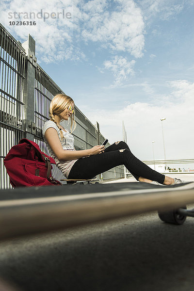 Teenager-Mädchen auf dem Skateboard sitzend mit dem Handy