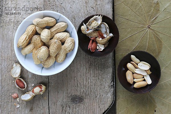 Erdnüsse  geschält und ungeschält  in verschiedenen Schälchen auf rustikalem Brett