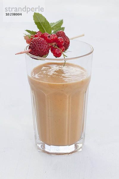 Kokos-Macadamia-Smoothie mit Erdbeeren im Glas  Holzspieß mit Früchten und Minze