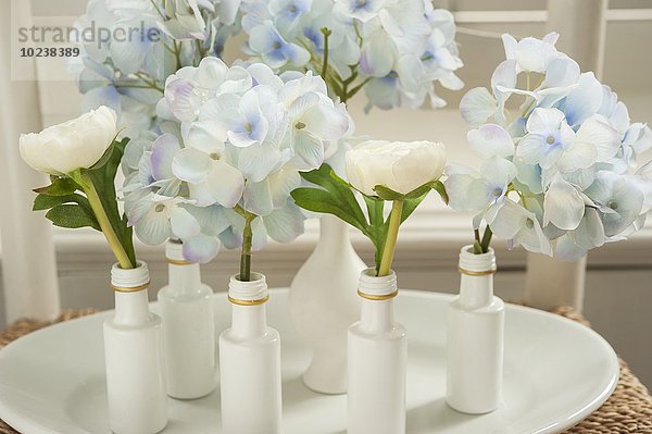 Hortensien und Ranunkeln in kleinen  weiss bemalten Flaschen und Vasen