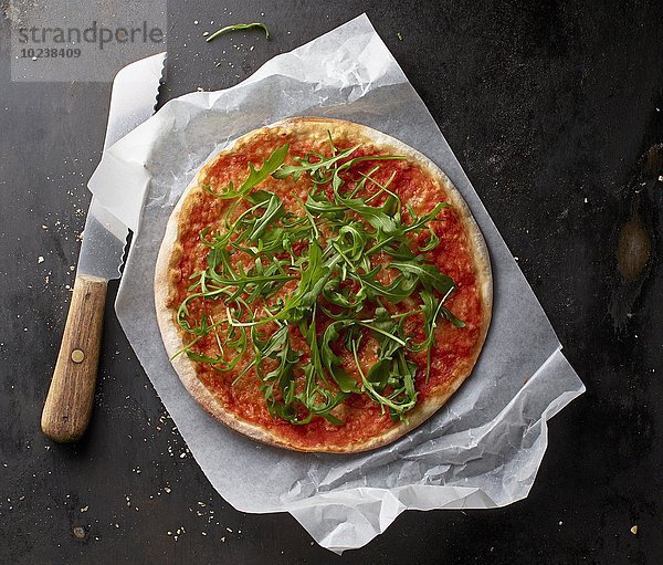 Pizza Margherita mit Rucola auf Papier mit Messer