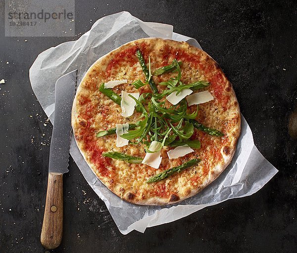 Pizza Margherita mit Spargel  Rucola und gehobeltem Parmesan auf Papier mit Messer