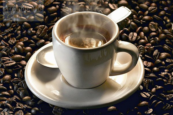 Dampfende Espressotasse auf gerösteten Kaffeebohnen