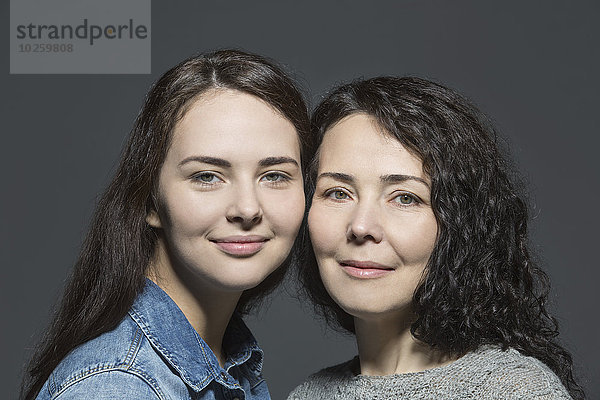 Porträt von lächelnder Mutter und Tochter vor übergrauem Hintergrund
