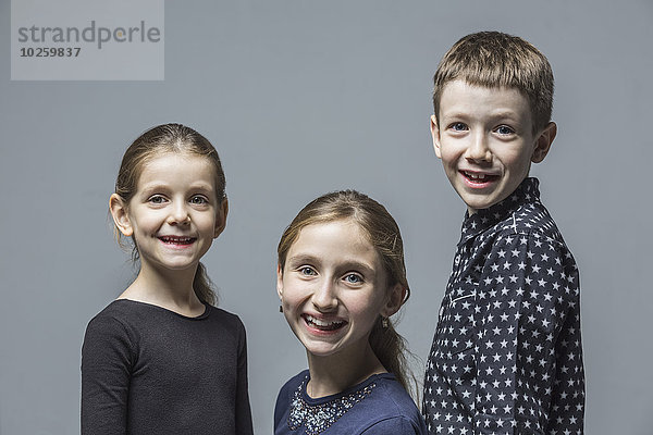 Porträt eines lächelnden Bruders mit Schwestern über grauem Hintergrund