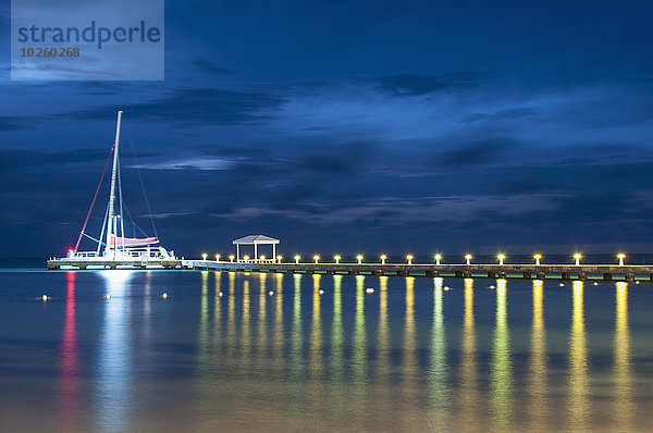 Segelboot am beleuchteten Pier auf dem See gegen den Himmel bei Nacht vertäut