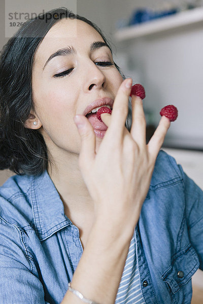 Junge Frau isst zu Hause Himbeeren an den Fingern