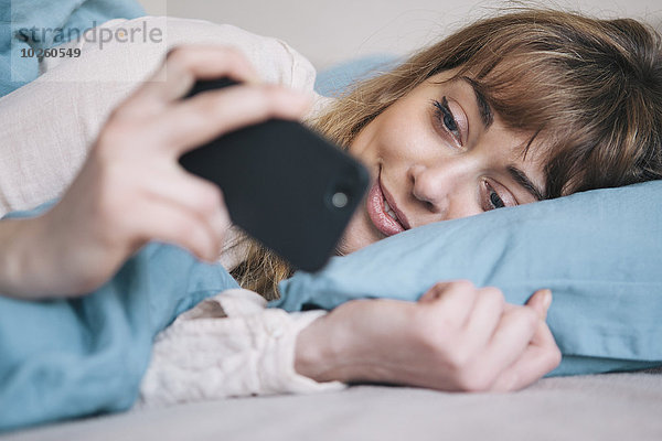 Junge Frau mit dem Handy im Bett entspannen