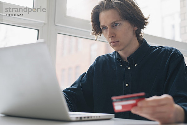 Junger Mann mit Kreditkarte und Laptop am Tisch
