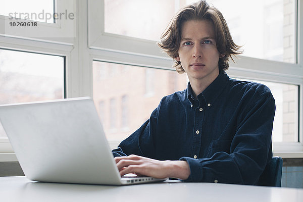 Porträt eines selbstbewussten jungen Mannes mit Laptop am Schreibtisch