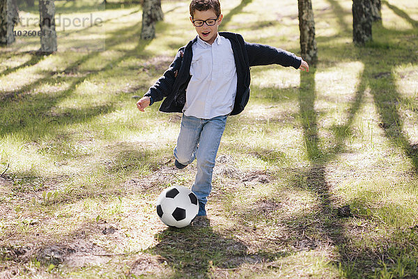 Volle Länge des fröhlichen Jungen beim Fußballspielen im Wald