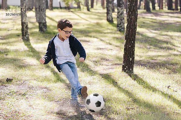 Volle Länge des fröhlichen Jungen beim Fußballspielen im Wald