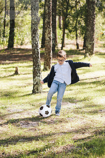 Volle Länge des Jungen beim Fußballspielen im Wald
