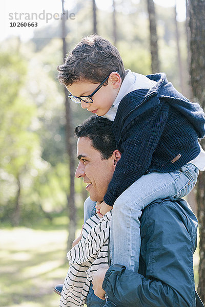 Lächelnder Mann mit Sohn auf den Schultern im Wald