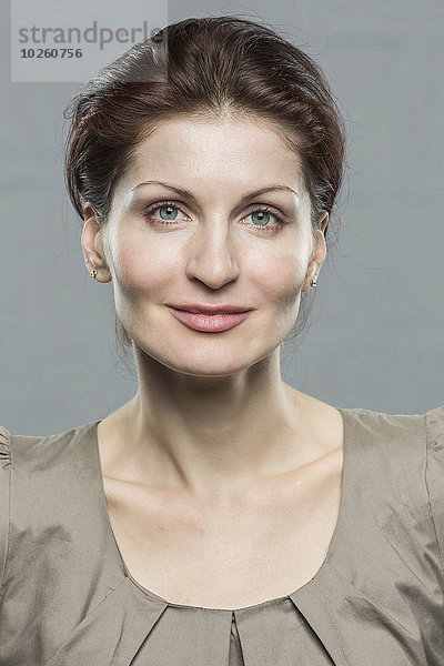 Porträt einer lächelnden mittleren erwachsenen Frau vor grauem Hintergrund