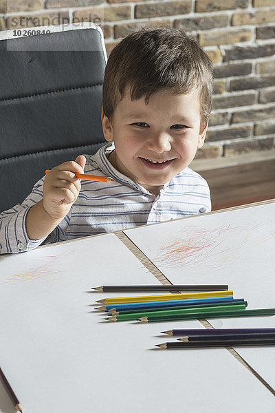 Porträt des glücklichen Jungen beim Zeichnen am Tisch im Haus